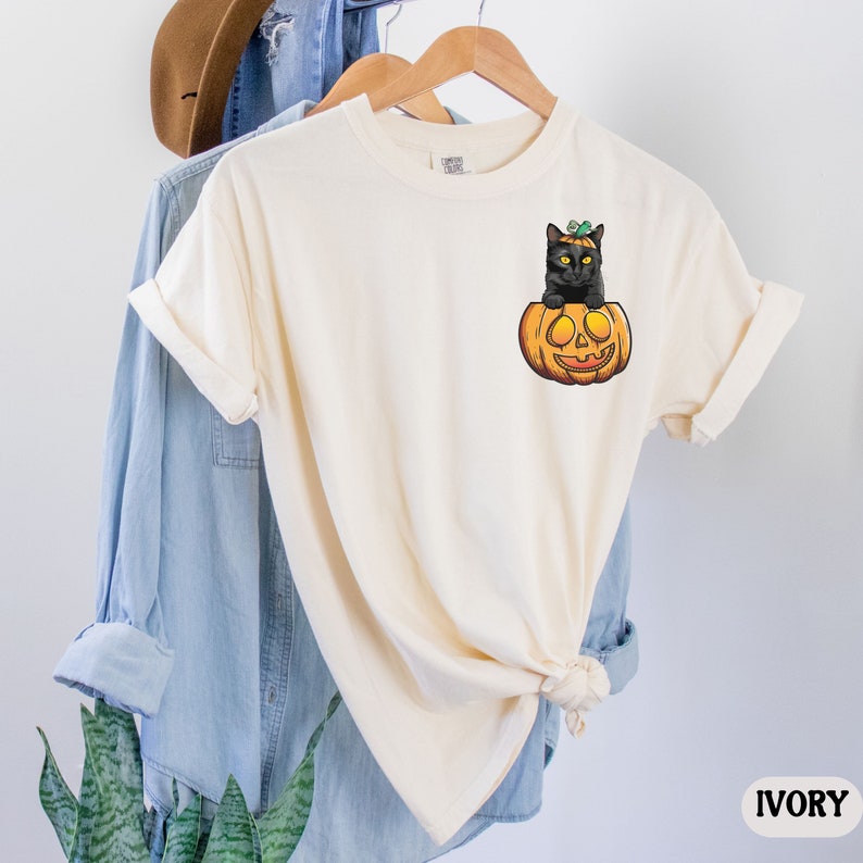 May include: A cream colored t-shirt with a black cat sitting inside a jack-o'-lantern. The text "IVORY" is in the bottom right corner of the image.