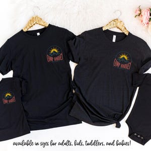 K&ouml;nnte beinhalten: Zwei schwarze T-Shirts mit kurzen &Auml;rmeln, ein Kinder-T-Shirt und ein Baby-Body. Jedes Kleidungsst&uuml;ck zeigt auf der Brust ein kreisf&ouml;rmiges Motiv mit einer gelben Sonne &uuml;ber dunklen Bergen und dem darunter gedruckten Text Camp Harvey.