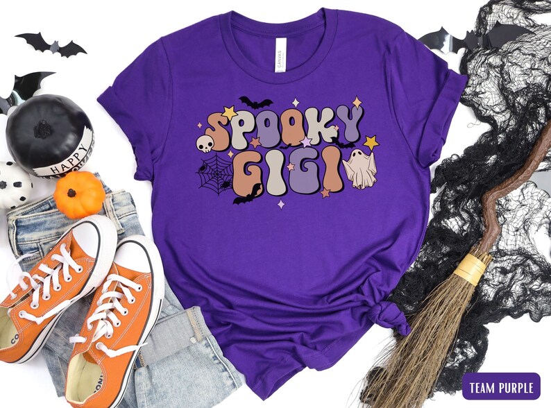 May include: Purple t-shirt featuring a graphic of the text "Spooky Gigi" in a retro font with a ghost and bats.