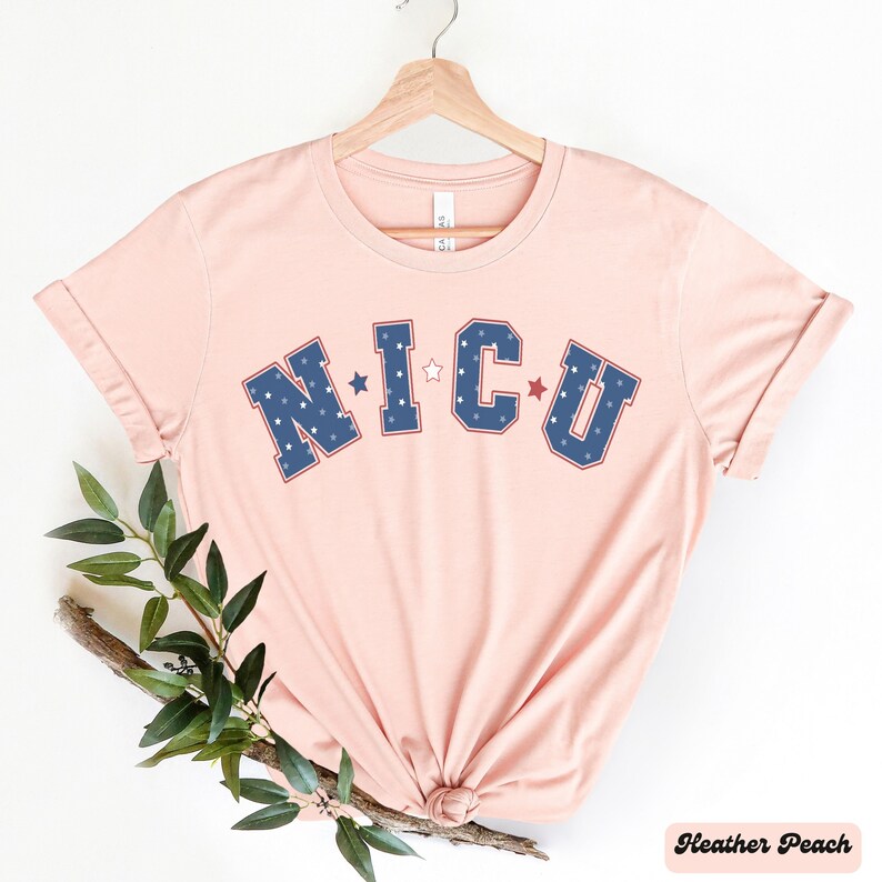 May include: A heather peach t-shirt with a blue and red "NICU" graphic with white stars. The graphic is in a collegiate style font.