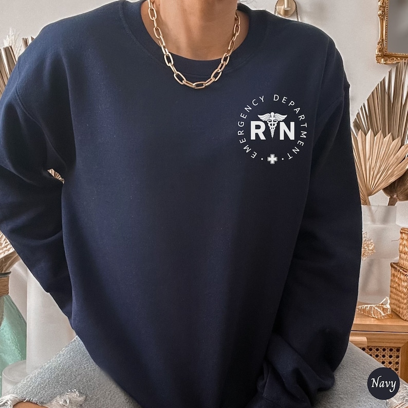 Peut inclure: Sweat-shirt bleu marine avec un graphique blanc d'un symbole m&eacute;dical et le texte "Emergency Department RN".