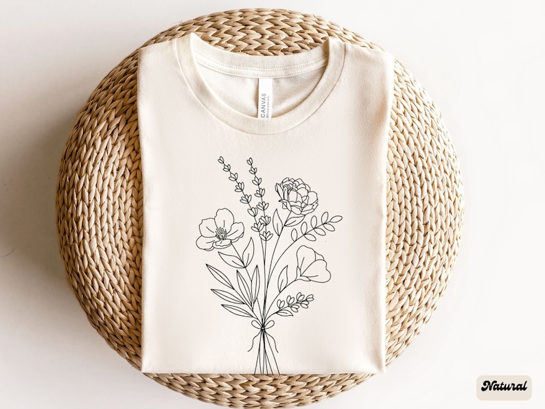 以下が含まれることがあります： 白いTシャツに、黒い線で描かれた花束のイラスト。花束には、バラ、ポピー、ラベンダーが含まれています。