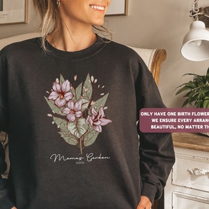 May include: Black sweatshirt with a floral design and the text "Mamas Garden ALKIA". The text below the design reads "ONLY HAVE ONE BIRTH FLOWER? NO WORRIES! WE ENSURE EVERY ARRANGEMENT IS BEAUTIFUL, NO MATTER THE NUMBER".