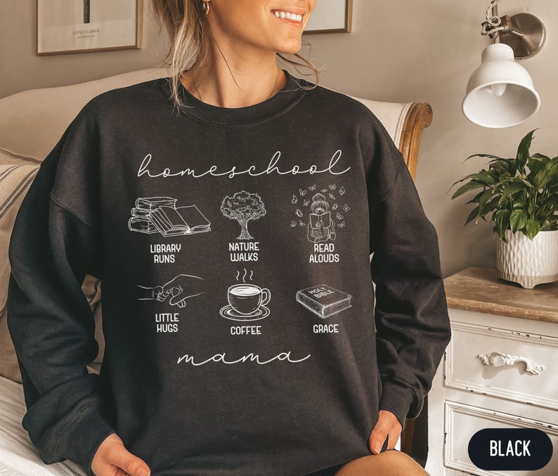 Puede incluir: Sudadera negra con texto blanco que dice "homeschool mama" e ilustraciones de libros, un &aacute;rbol, una persona leyendo, una taza de caf&eacute; y un libro con la palabra "grace" en &eacute;l. Las ilustraciones est&aacute;n dispuestas en una cuadr&iacute;cula.