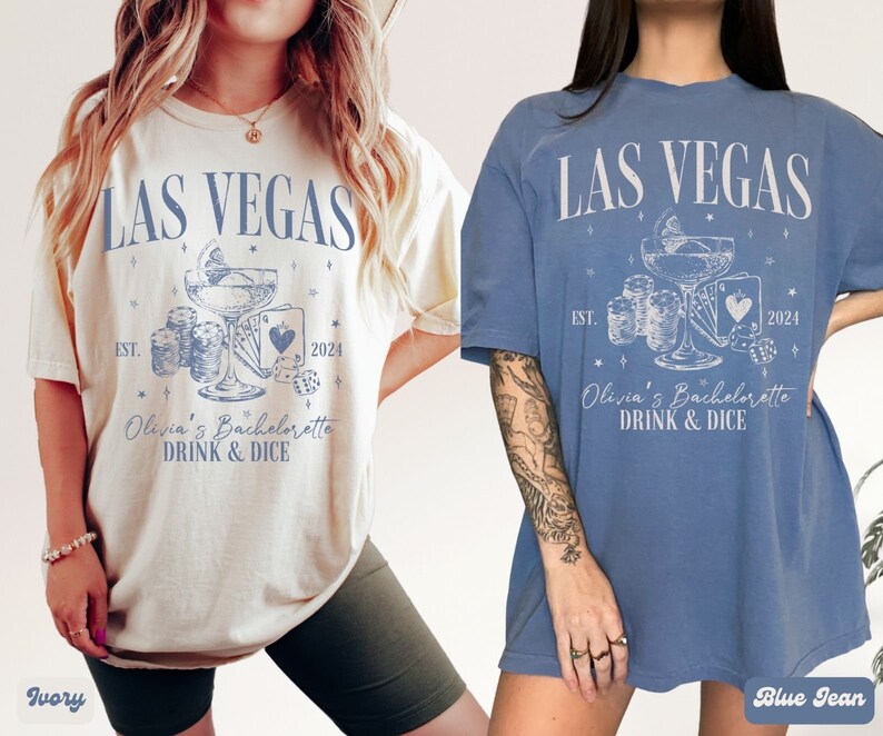 May include: Two t-shirts with a Las Vegas theme. The shirts are in ivory and blue jean colors. The design features a cocktail glass with dice and playing cards. The text on the shirts reads "Las Vegas" and "Olivia's Bachelorette Drink & Dice".