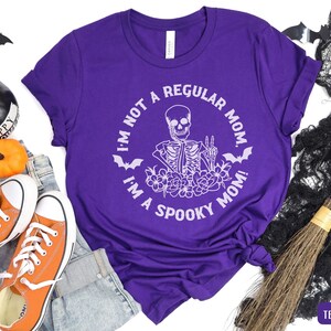May include: Purple t-shirt with a white skeleton graphic and the text "I'm not a regular mom, I'm a spooky mom!"