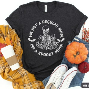 May include: Dark grey heather t-shirt with a white graphic of a skeleton with flowers and bats. The text on the shirt reads "I'm not a regular mom. I'm a spooky mom!"