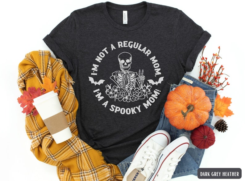 May include: Dark grey heather t-shirt with a white graphic of a skeleton with flowers and bats. The text on the shirt reads "I'm not a regular mom. I'm a spooky mom!"