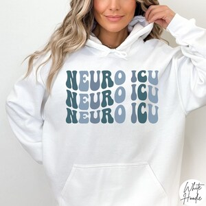 Pode incluir: Camisola de capuz branca com o texto "NEURO ICU" repetido tr&ecirc;s vezes numa fonte retro azul e verde.