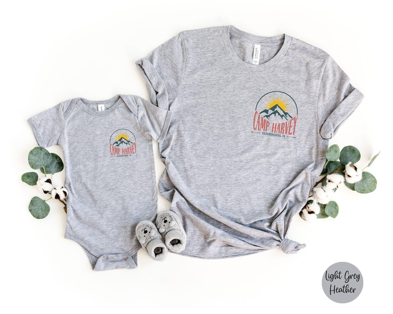 K&ouml;nnte beinhalten: Ein hellgrau meliertes T-Shirt und ein passender Baby-Body, beide mit einer kreisf&ouml;rmigen Grafik auf der Brust, die eine gelbe Sonne, blaue Berge und den roten Schriftzug "CAMP HARVEY" sowie darunter "PENNSYLVANIA, PA" in kleiner schwarzer Schrift zeigt.
