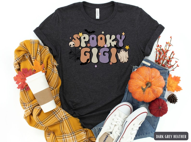 May include: Dark grey heather t-shirt featuring a retro-style graphic that says "Spooky Gigi" in colourful letters. The graphic also includes a ghost, a spider web, and bats.