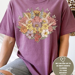 Pode incluir: T-shirt cor de baga com um design de buqu&ecirc; floral em tons de rosa, amarelo e azul. O texto na imagem diz: "WE CAN ADD UP TO 30 BIRTH MONTH FLOWERS TO YOUR BOUQUET DESIGN".