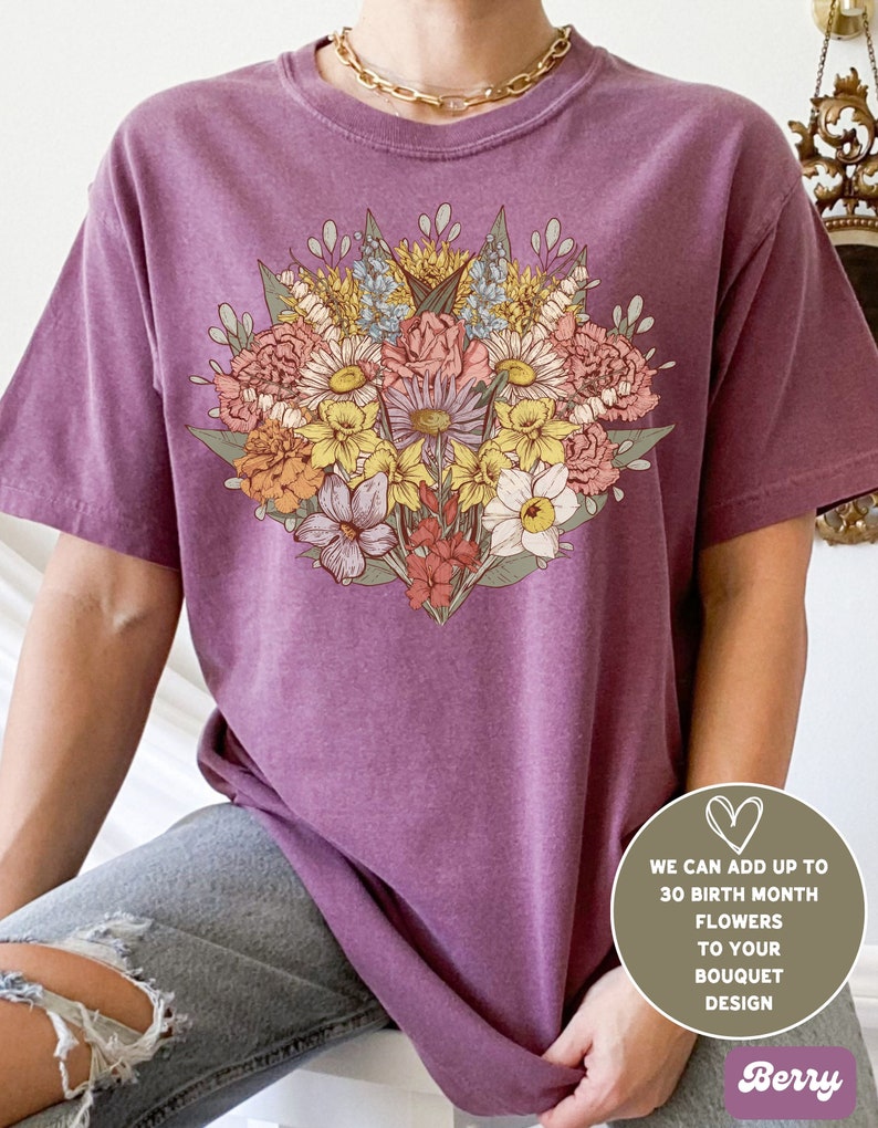 Pode incluir: T-shirt cor de baga com um design de buqu&ecirc; floral em tons de rosa, amarelo e azul. O texto na imagem diz: "WE CAN ADD UP TO 30 BIRTH MONTH FLOWERS TO YOUR BOUQUET DESIGN".