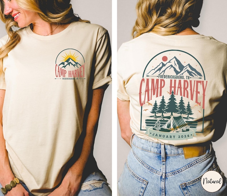 K&ouml;nnte beinhalten: Ein cremefarbenes Kurzarm-T-Shirt mit einem Grafikdesign. Auf der Brust befindet sich ein Berg- und Sonnenlogo mit dem Text Camp Harvey Fredericksburg, TX. Die R&uuml;ckseite zeigt eine gr&ouml;&szlig;ere Version derselben Berg-, Wald- und Zelt-Szene.