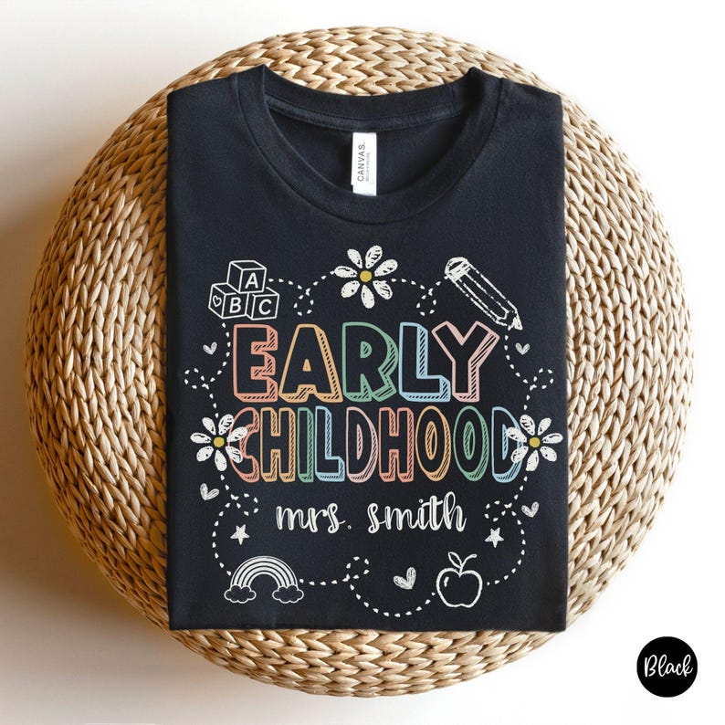 Pode incluir: T-shirt preta com a frase "EARLY CHILDHOOD" em letras coloridas, rodeada por ilustra&ccedil;&otilde;es brancas de flores, um l&aacute;pis, blocos ABC, um arco-&iacute;ris e uma ma&ccedil;&atilde;. O texto "mrs. smith" est&aacute; abaixo.