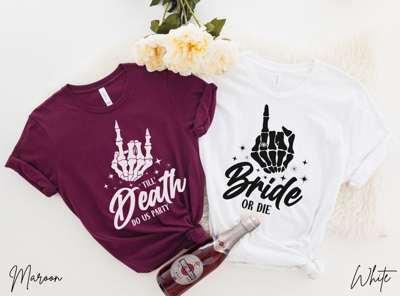 Puede incluir: Dos camisetas con un dise&ntilde;o de mano de esqueleto. La camiseta granate dice "Till Death Do Us Party" y la camiseta blanca dice "Bride or Die".
