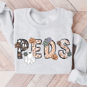 May include: A light gray sweatshirt with the word "PEDS" in a Halloween-themed design. The letters are decorated with pumpkins, ghosts, and floral accents. The sweatshirt has long sleeves.