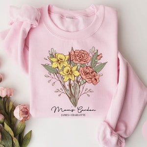 May include: Light pink sweatshirt with a floral design and the text "Mommy's Garden" with the names "James & Charlotte" underneath.