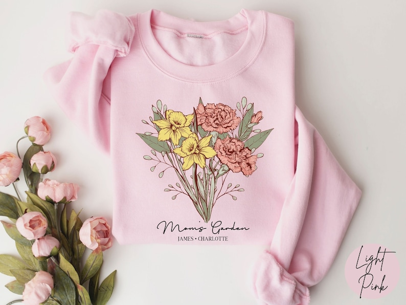 May include: Light pink sweatshirt with a floral design and the text "Mommy's Garden" with the names "James & Charlotte" underneath.