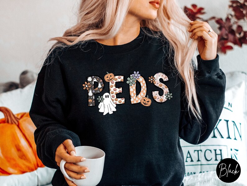 May include: Black sweatshirt with the word "PEDS" in a decorative font. The letters are filled with Halloween-themed patterns, including pumpkins, ghosts, and flowers. The sweatshirt is a crew neck style.