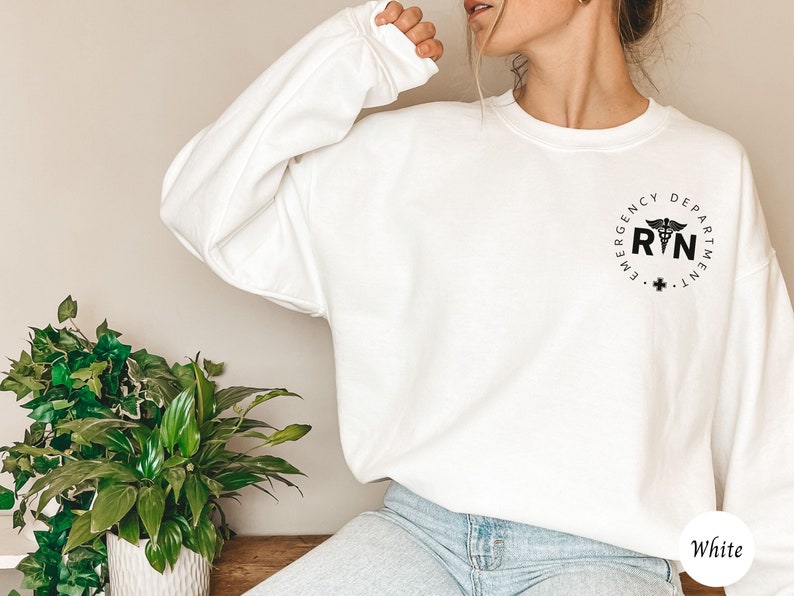 Peut inclure: Sweat-shirt blanc avec un graphique noir et blanc d'un symbole m&eacute;dical et le texte "Emergency Department RN" dans un cercle.