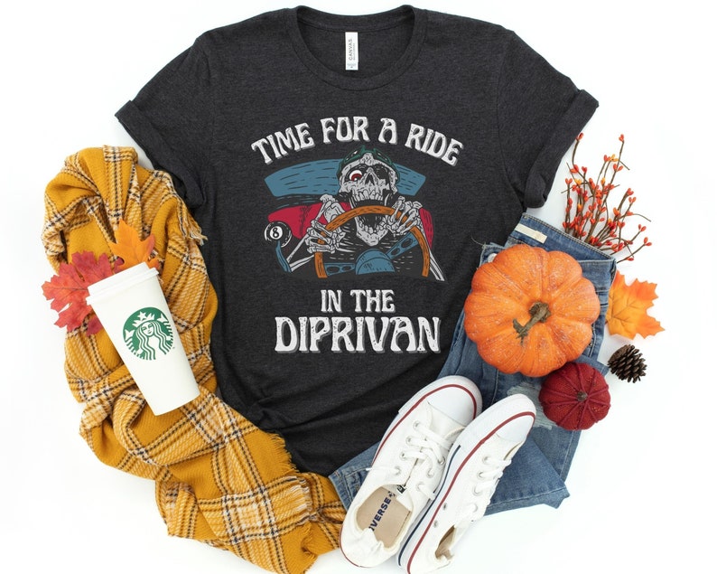 May include: A dark gray t-shirt with a graphic of a skeleton driving a car. The text on the shirt reads "Time for a ride in the dip-rivan".