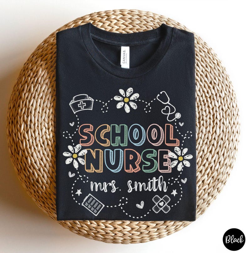Puede incluir: Camiseta negra con la frase "SCHOOL NURSE" en letras coloridas, rodeada de margaritas, un estetoscopio y s&iacute;mbolos m&eacute;dicos. El nombre "mrs. smith" est&aacute; debajo. La camiseta es de lona.