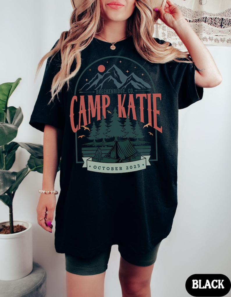 May include: Black oversized t-shirt with a graphic design of a mountain range, a tent, and trees. The text "Breckenridge Co. Camp Katie October 2023" is printed on the shirt.
