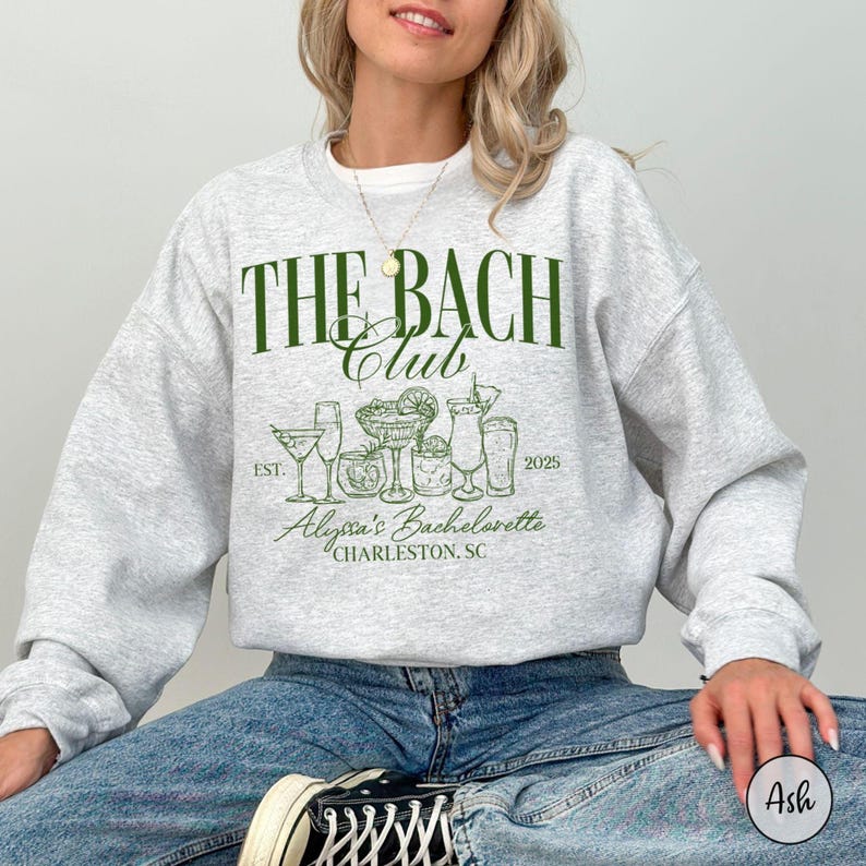K&ouml;nnte beinhalten: Ein grauer Pullover mit dem Text "The Bach Club" in gr&uuml;ner Schrift. Der Text "Est. 2025" befindet sich unter dem Clubnamen. Der Text "Alyssa's Bachelorette Charleston, SC" befindet sich unter dem Datum.