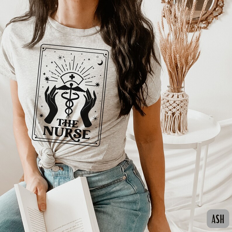 May include: A grey t-shirt with a black graphic of a tarot card featuring a caduceus and the text "THE NURSE".