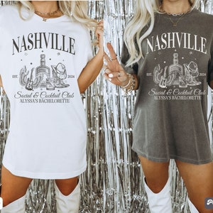 K&ouml;nnte beinhalten: Zwei wei&szlig;e T-Shirts mit einem schwarzen Grafikdesign. Die Grafik zeigt eine Flasche Alkohol, einen Cowboyhut, eine Gitarre und den Text "Nashville Social & Cocktail Club Alyssa's Bachelorette Est. 2024". Ein Shirt ist wei&szlig; und das andere ist dunkelgrau.