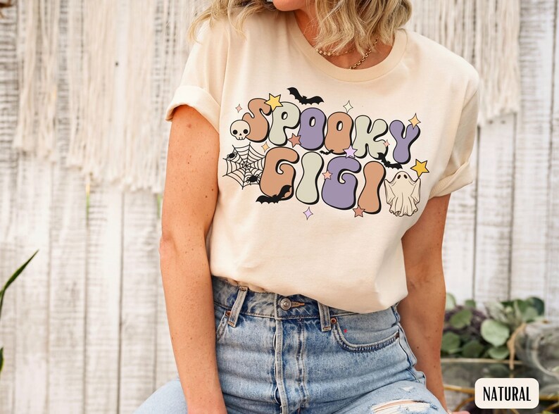 May include: A cream coloured t-shirt with a retro-style graphic that says "Spooky Gigi" in colourful letters. The graphic also includes a ghost, bats, and a spider web.