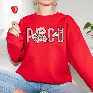 Peut inclure: Sweat-shirt rouge avec un ourson rose tenant une lettre et le mot "POCU" imprim&eacute; sur le devant.
