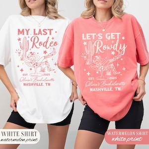 May include: Two oversized t-shirts with a bachelorette party theme. The white shirt has a watermelon pink print that says "My Last Rodeo" with a cactus and a woman in a cowboy hat sitting in a glass. The watermelon shirt has a white print that says "Let's Get Rowdy" with a cactus and a woman in a cowboy hat sitting in a glass.