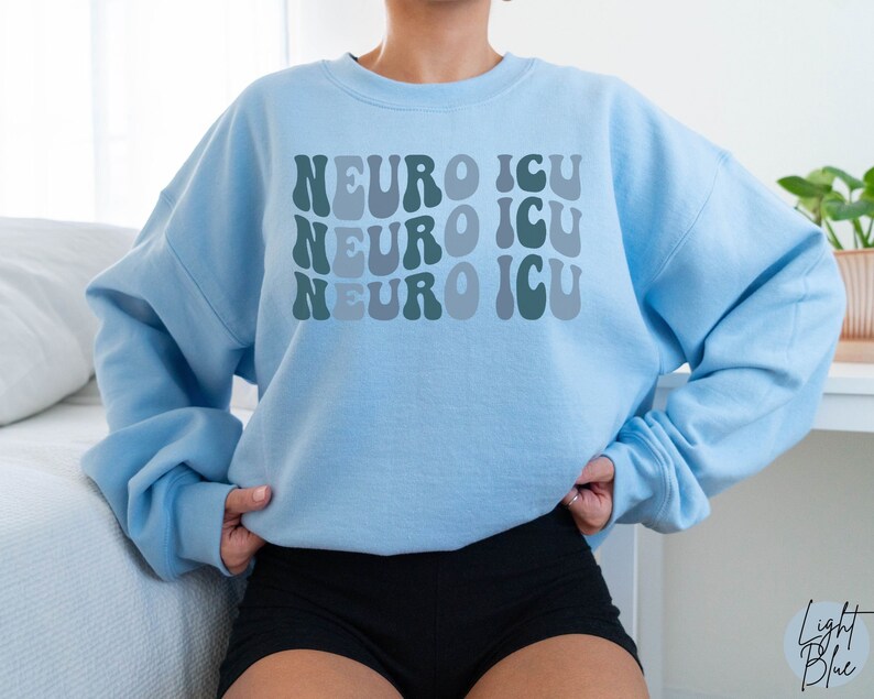 Pode incluir: Camisola azul claro com o texto "Neuro ICU" repetido tr&ecirc;s vezes em uma fonte retr&ocirc; e ondulada. O texto est&aacute; em tons de verde e azul.