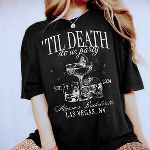 Puede incluir: Camiseta negra con texto blanco que dice 'Til Death Do Us Party' con un gr&aacute;fico de calavera y huesos cruzados y el texto 'Alyssa's Bachelorette Las Vegas, NV'.