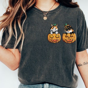 May include: A dark grey t-shirt featuring a graphic of two calico cats peeking out of jack-o'-lantern pumpkins.