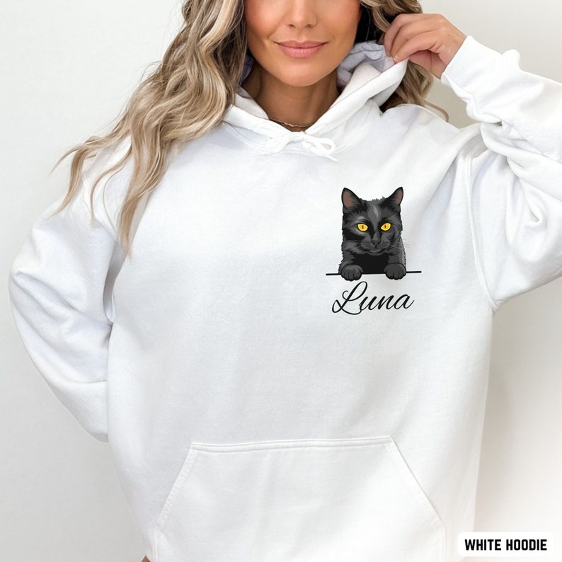Puede incluir: Sudadera con capucha blanca con un gato negro asom&aacute;ndose del bolsillo y el nombre "Luna" escrito debajo. La sudadera tiene un bolsillo canguro.