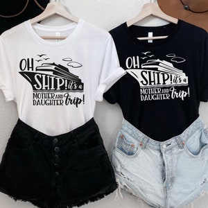May include: Two t-shirts featuring a cruise ship graphic and the text "Oh Ship! It's a Mother and Daughter Trip!" One shirt is white with black text and the other is black with white text.