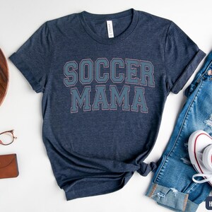 May include: A heather navy blue t-shirt with the text "Soccer Mama" in white with a light blue outline.