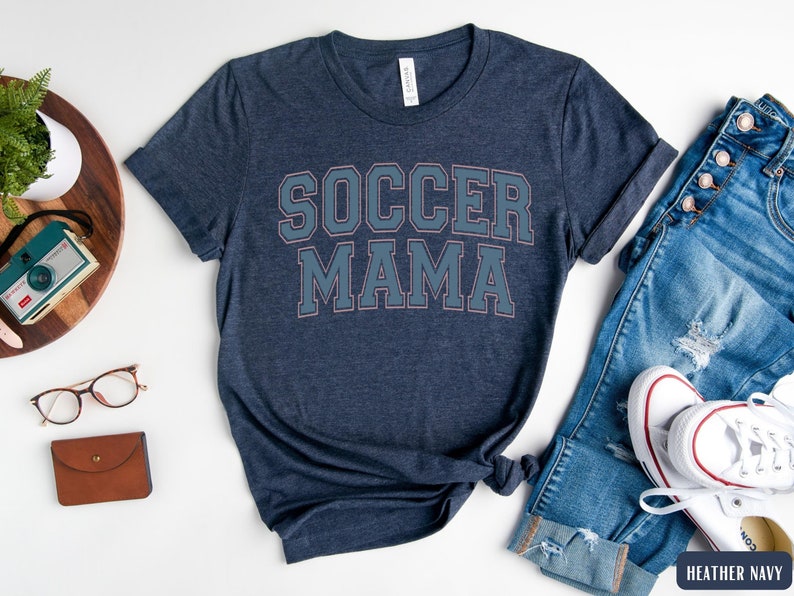 May include: A heather navy blue t-shirt with the text "Soccer Mama" in white with a light blue outline.