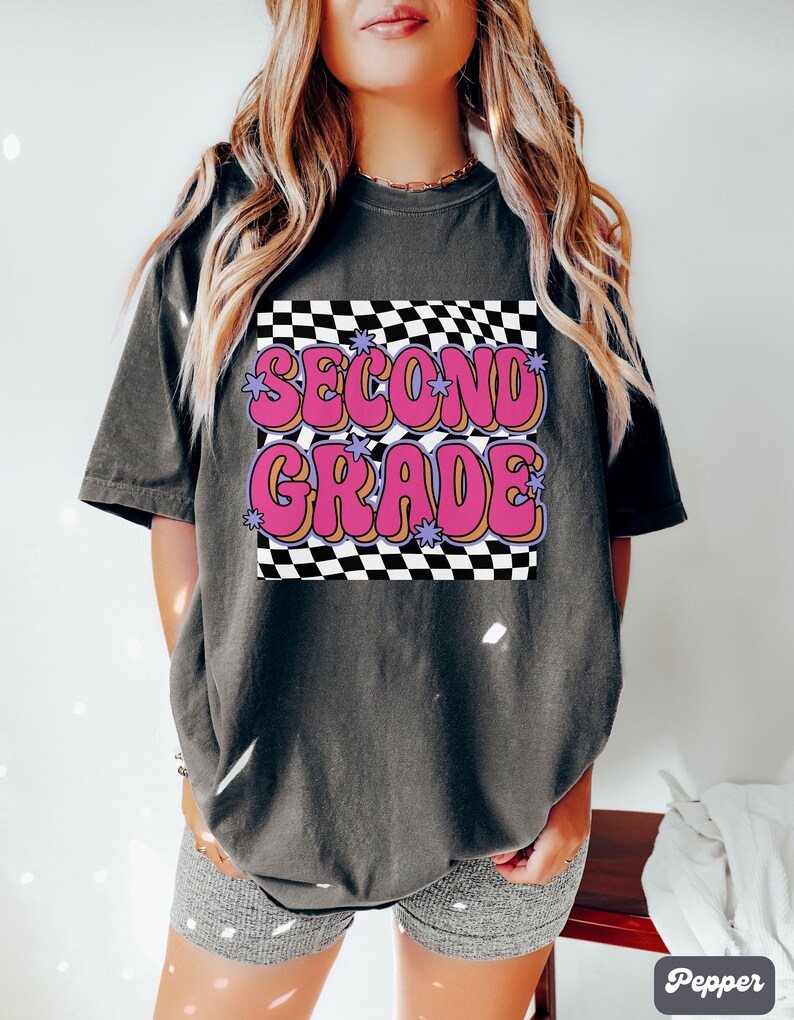 以下が含まれることがあります： 黒っぽいグレーのTシャツに、市松模様と「SECOND GRADE」という文字がピンクと紫の文字で書かれている。