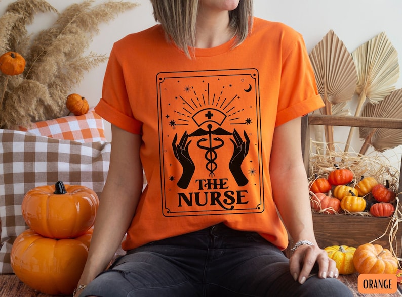 May include: Orange t-shirt featuring a black graphic of a tarot card that reads "The Nurse" with a medical caduceus symbol.