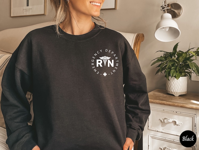 Peut inclure: Sweat-shirt noir avec un graphique blanc d'un symbole m&eacute;dical et le texte "Emergency Department RN".