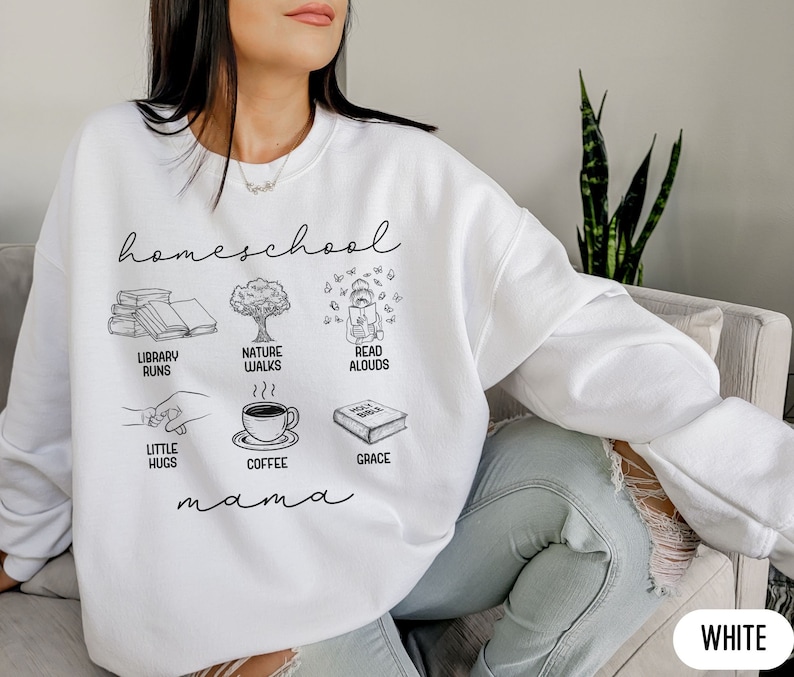 Puede incluir: Sudadera blanca con el texto "homeschool mama" e ilustraciones de libros, un &aacute;rbol, un ni&ntilde;o leyendo, caf&eacute; y un abrazo.