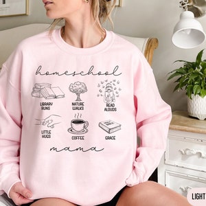Puede incluir: Sudadera rosa claro con el texto "homeschool mama" e ilustraciones de libros, caf&eacute;, paseos por la naturaleza, lectura en voz alta y peque&ntilde;os abrazos.