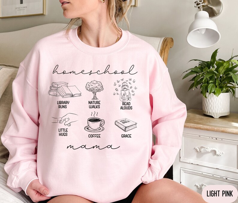 Puede incluir: Sudadera rosa claro con el texto "homeschool mama" e ilustraciones de libros, caf&eacute;, paseos por la naturaleza, lectura en voz alta y peque&ntilde;os abrazos.