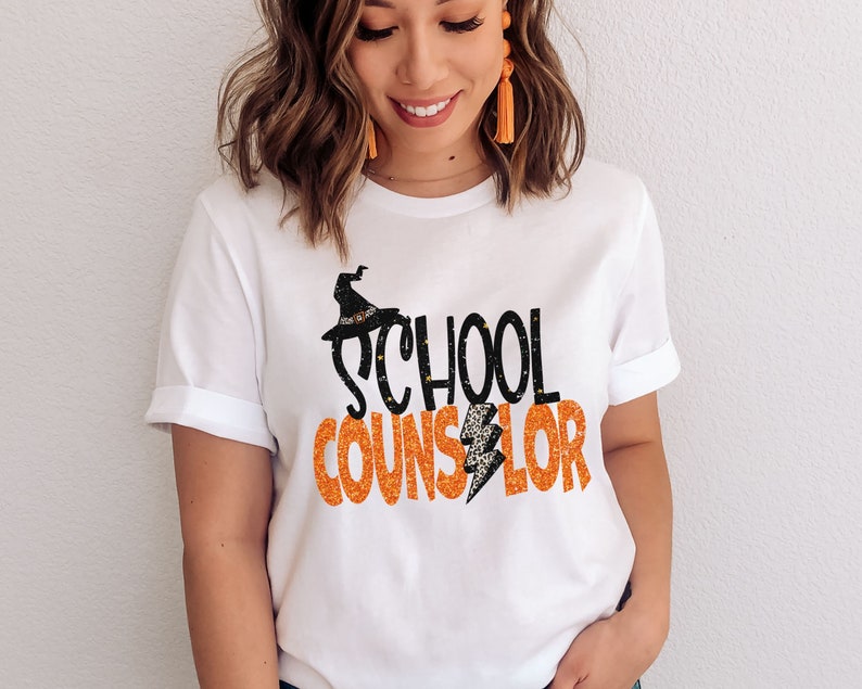 May include: White t-shirt with the text "SCHOOL COUNSELOR" in orange glitter letters with a black witch hat and lightning bolt graphic.