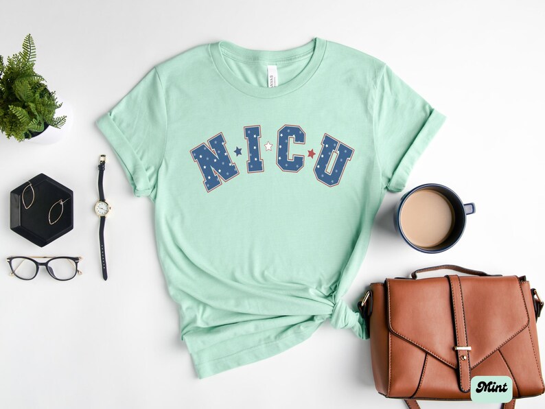 May include: A light green t-shirt with the text "NICU" in blue and red lettering with white stars. The letters are outlined in white.