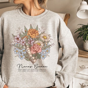 May include: A gray sweatshirt with a floral design and the text "Nana's Garden" with a list of names underneath.